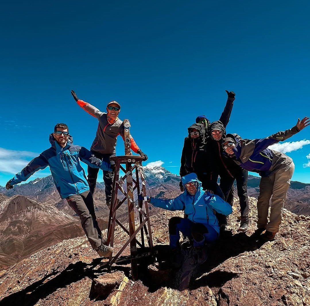 Grupo festejando en la cumbre, con la cordillera nevada de fondo